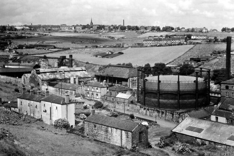A panoramic view over part of Morley from Morley Main pit tip behind old Morley gasworks. Valley Road can be seen in the foreground going diagonally across the picture from bottom right, with Valley Mills just starting on the right at the side of the gasworks. Most of the land in the middle distance is farmed as rhubarb fields with several sets of rhubarb forcing sheds being visible. 