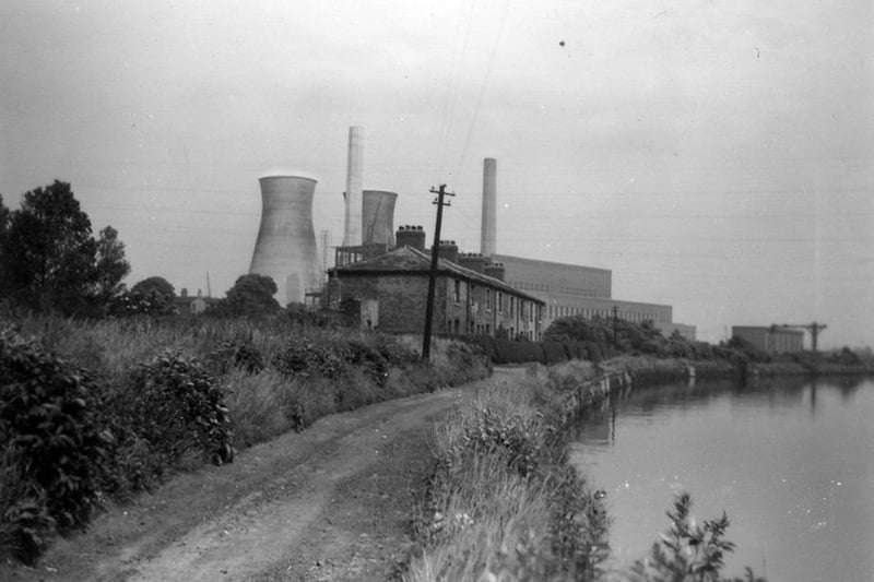 The cottages at Dandy Row, Thwaite, alongside the River Aire. Dandy Row housed workers at Thwaite Mills, and was effectively an island, surrounded by the River Aire, the Aire & Calder Navigation, and the mill stream. They feature id displays at Thwaite Mills, now a museum, and were demolished in 1968. Skelton Grange 'A' power station is visible behind the cottages, with two cooling towers at this time.
