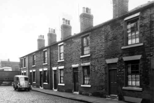 Single fronted back-to-back houses on Chambers Street, numbers run from 22 to 12, left to right. Across the wall on the left edge is a Leeds Corporation bus depot. A royal mail delivery van is parked outside number 20 Chambers Street. Pictured in October 1958.