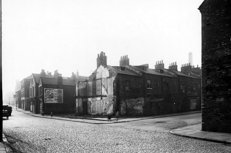 A view looking south from Carlton Street junction at Camp Road in October 1950. Several rows of terraced houses, some with windows are boarded up. One house has been demolished. An advertising hoarding for 'Heinz Baked Beans' appears on the side of one of the houses. There are also several children playing on the pavements. There is a pub by Primrose Street called the Royal George.