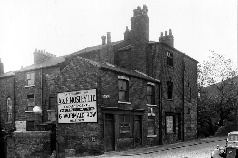 A view looking south west at Camp Road which backs onto Brunswick Place. The three terrace houses on Camp Road are abandoned with most windows either smashed, boarded up or bricked up. An advertising hoarding for 'A & F Mosley Ltd, Estate Agents, Insurance Agents' is fixed to the side of the row of houses. Pictured in October 1955.