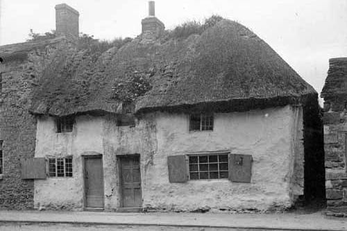 These thatched cottages, on two storeys, were located in Main Street. The one on the right, and possibly both, were used by a group of artists around the turn of the nineteenth century. They produced a Christmas Card in 1899 with a pen and ink drawing of this cottage, with the words 'From Ye Attic Abode'. They also each signed their initials in monogram style.  Pictured in July 1909.