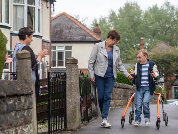 Tobias Weller, who has cerebral palsy and autism, is cheered on by neighbours as he walks along the street outside his home in Sheffield in his bid to raise cash for charity. Pic: Joe Giddens/PA Wire